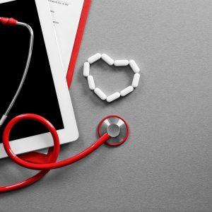Red stethoscope with tablet on grey table